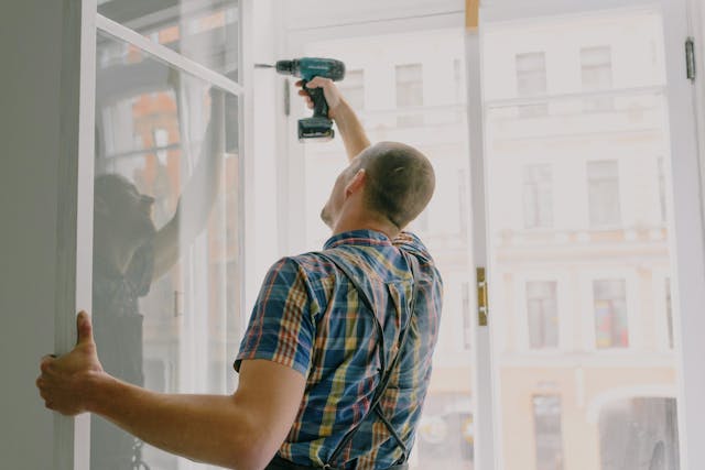 Person using a drill while holding up a window